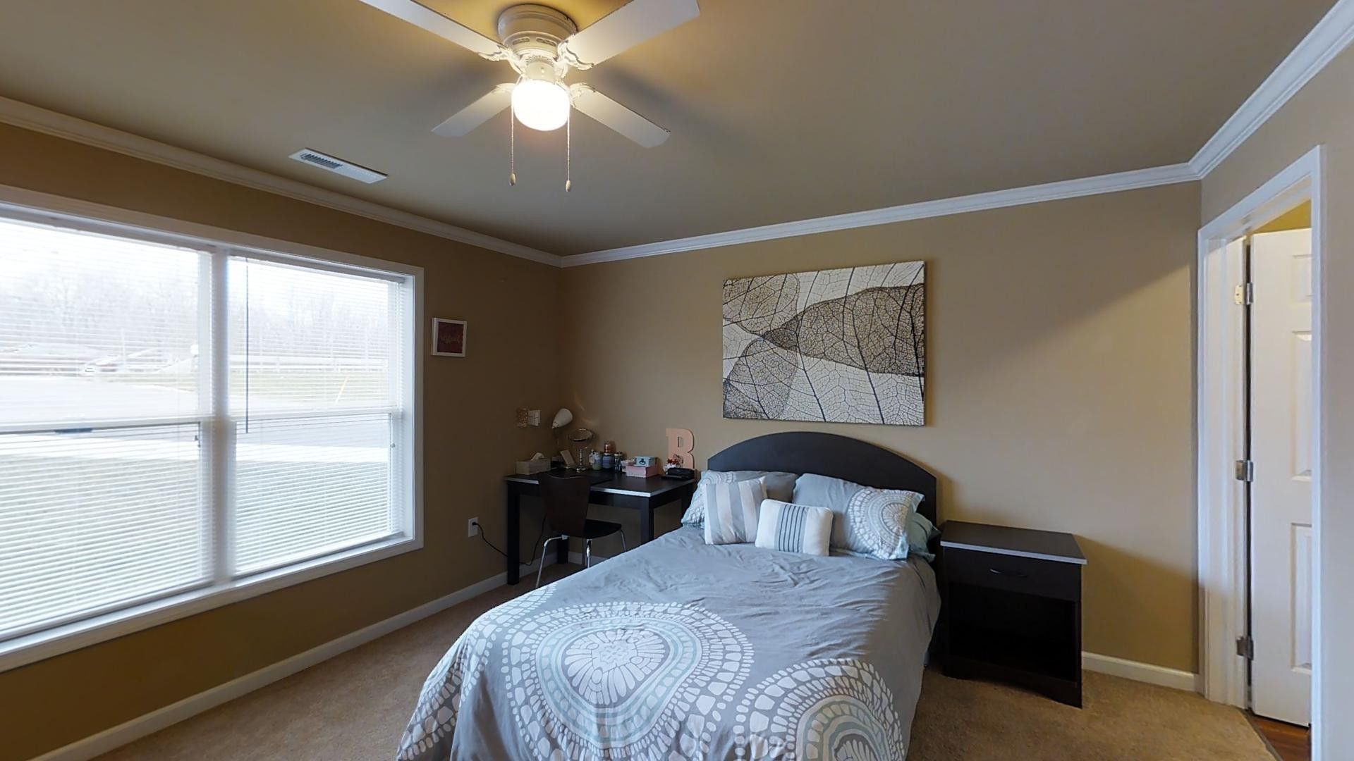 A bedroom with a bed , nightstand , desk and ceiling fan.