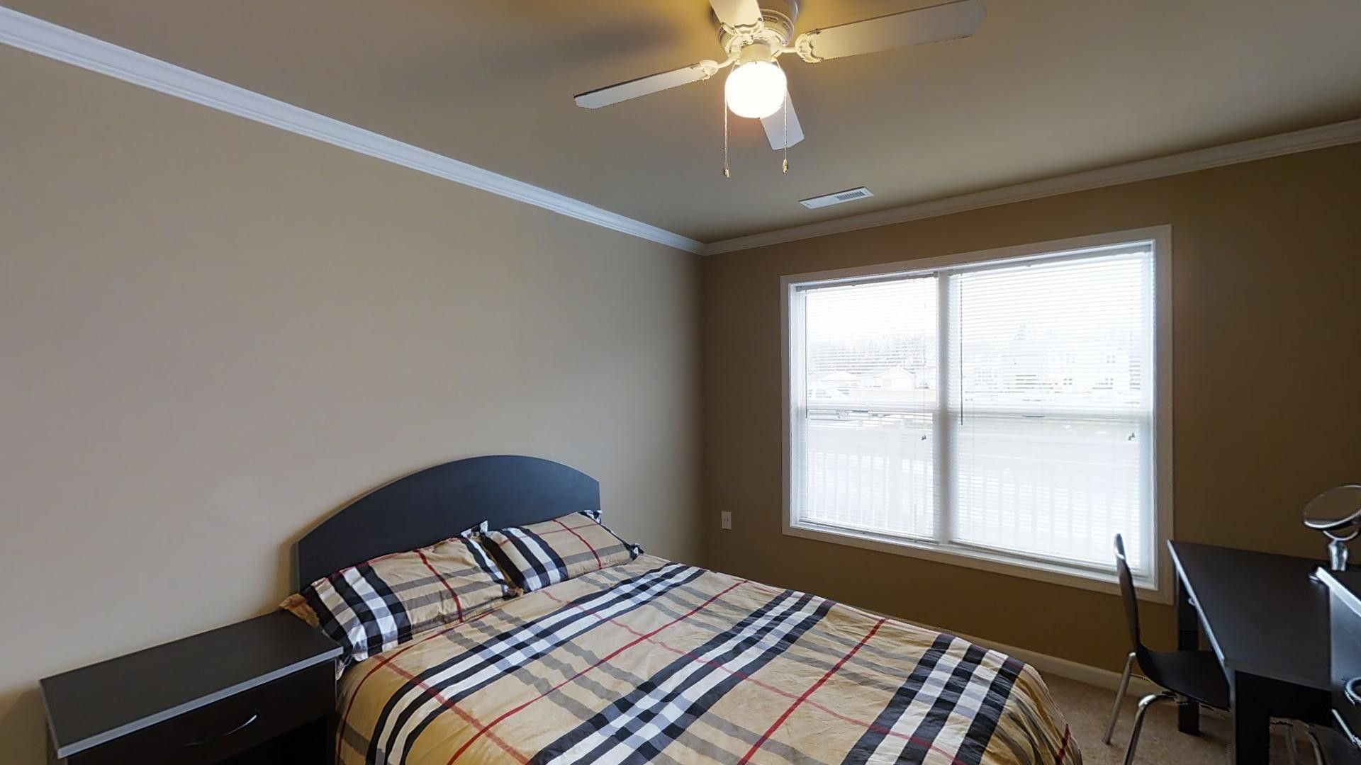 A bedroom with a bed , desk and ceiling fan.