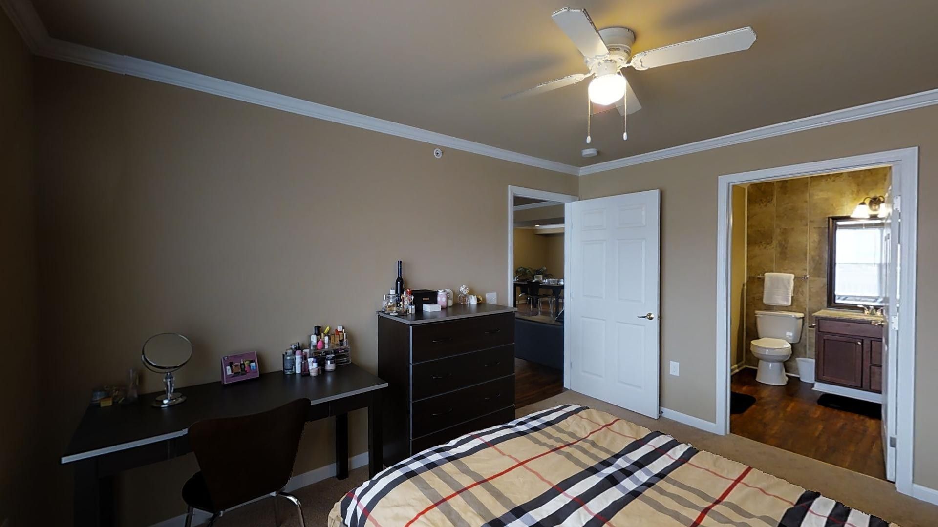 A bedroom with a bed , desk , chair and ceiling fan.