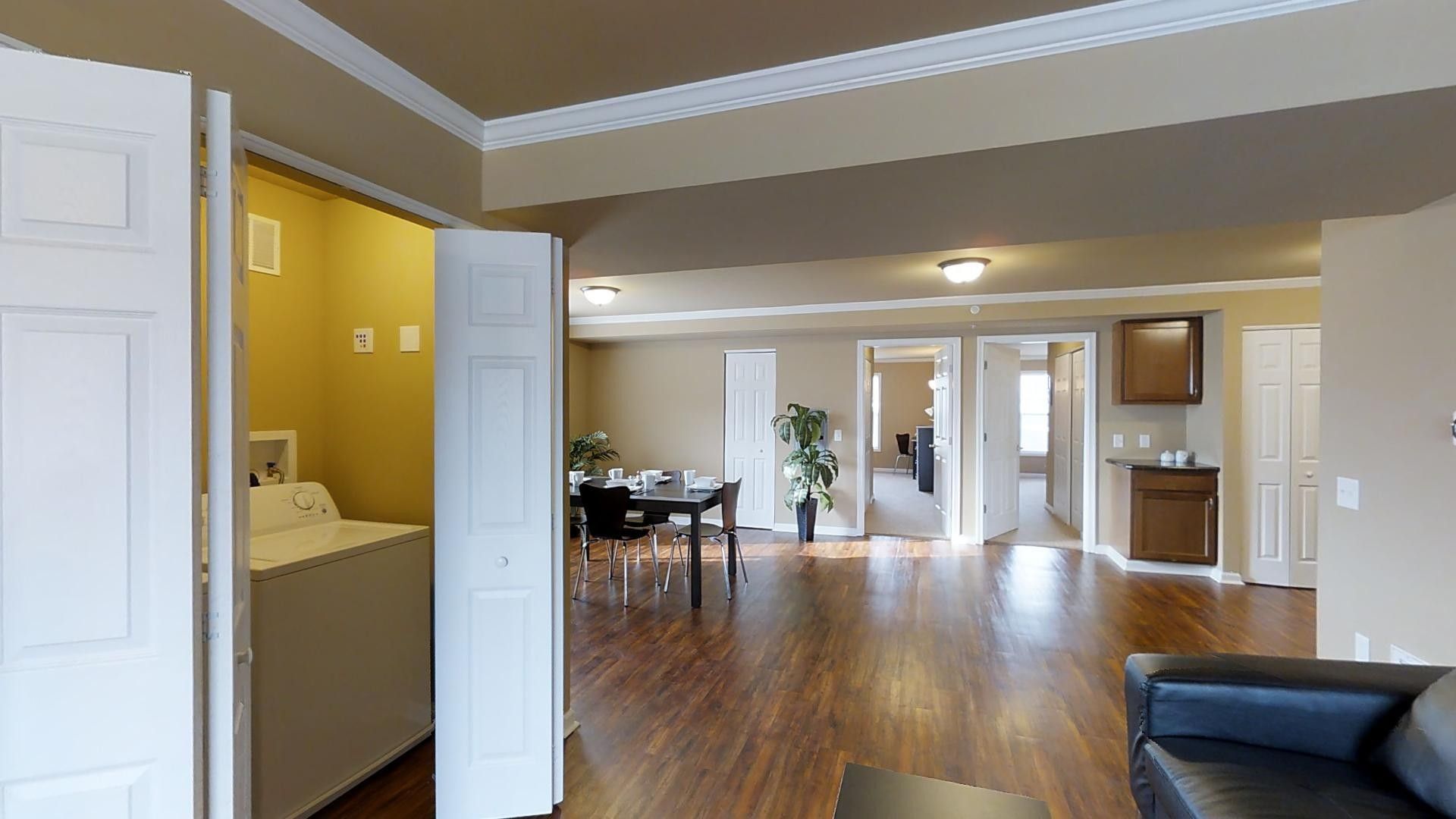 A living room with hardwood floors , a couch , a table and a laundry room.