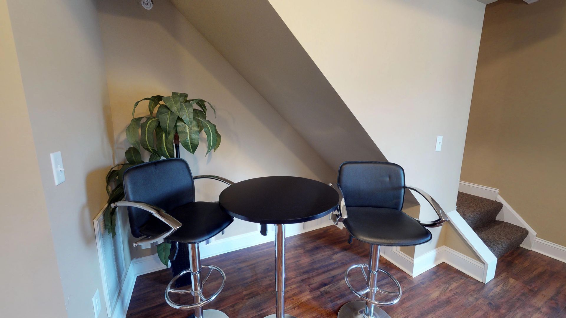 A room with two chairs and a table under a staircase.
