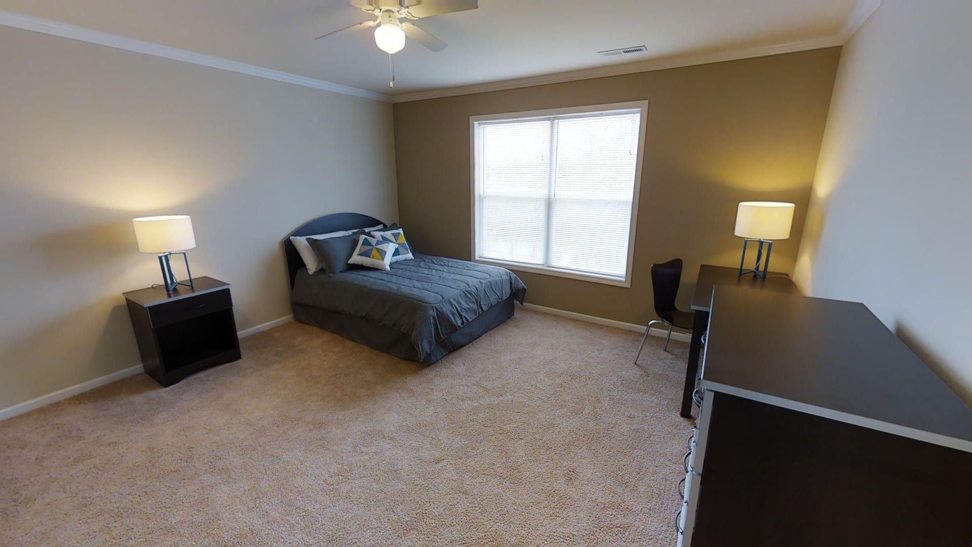 A bedroom with a bed , nightstand , desk and ceiling fan.
