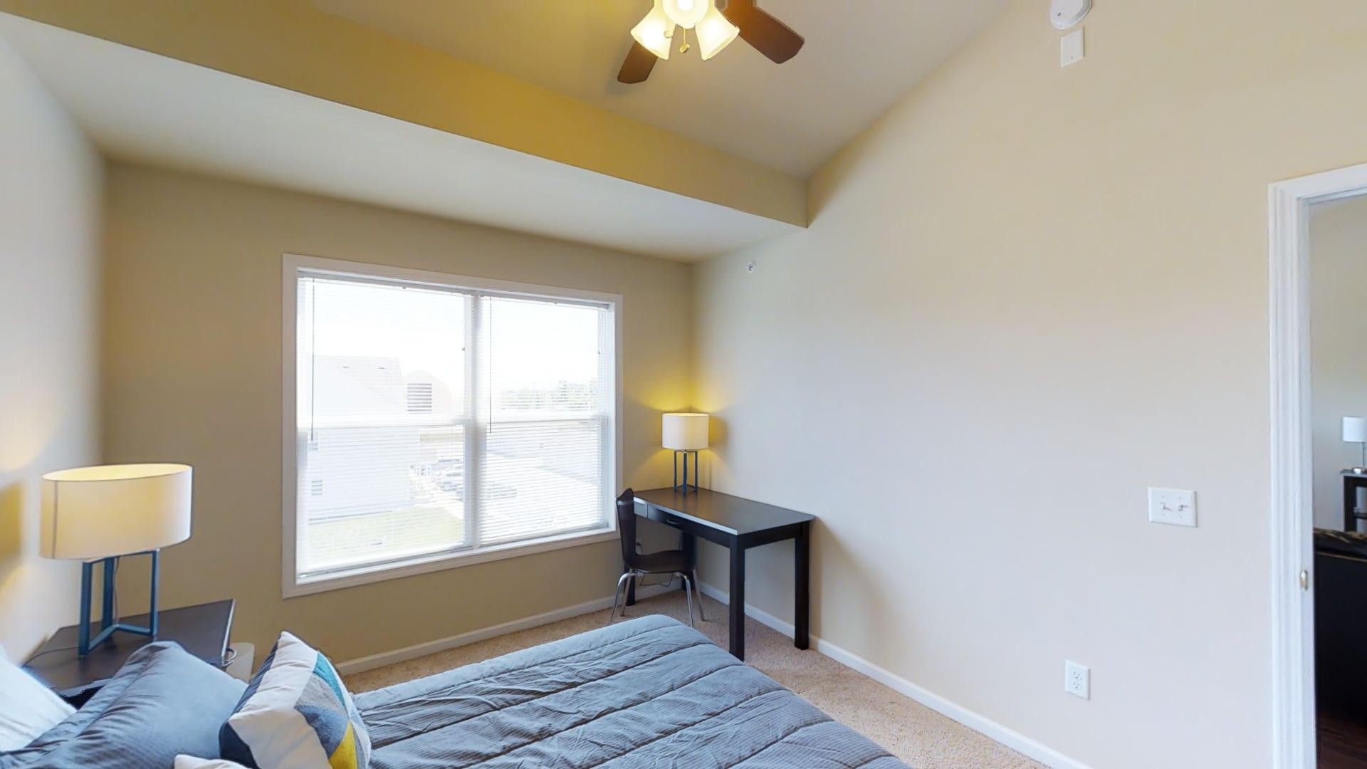 A bedroom with a bed , desk , lamps and a ceiling fan.