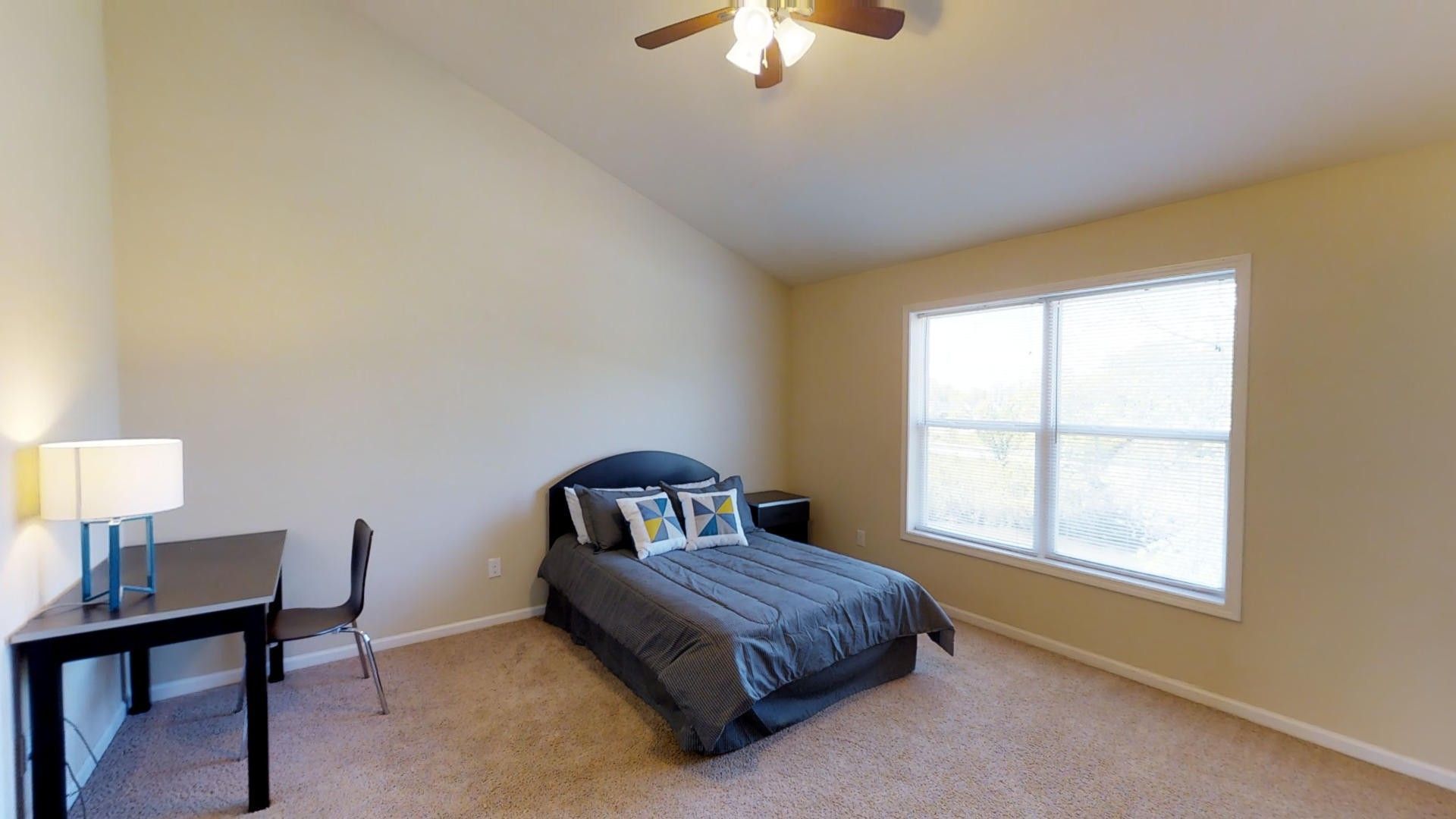 A bedroom with a bed , desk , chair and ceiling fan.