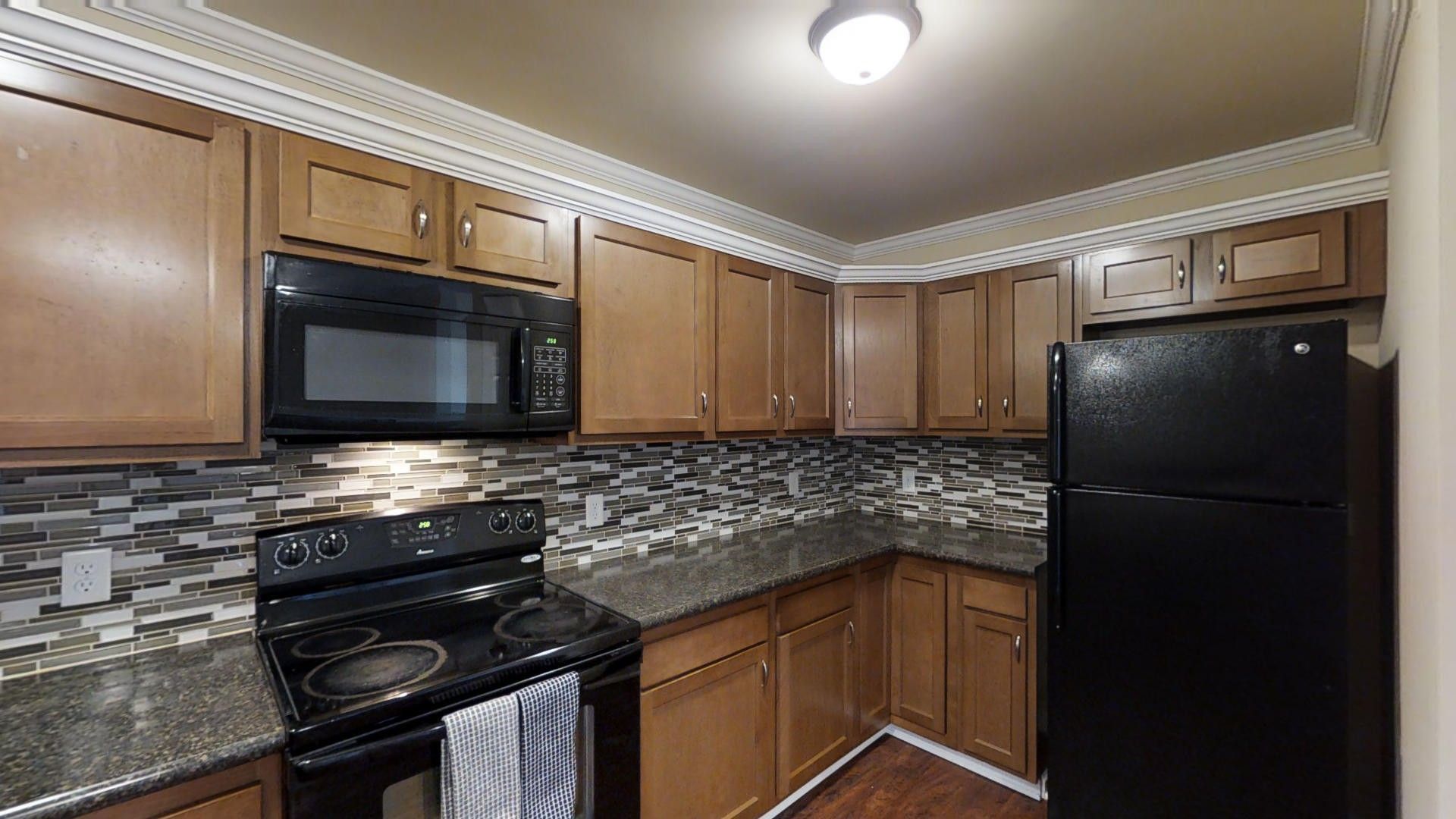 A kitchen with a black refrigerator , stove , microwave and cabinets.