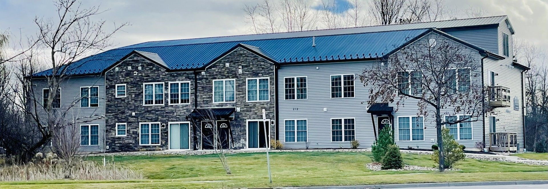 A large apartment building with a blue roof is surrounded by trees and grass.