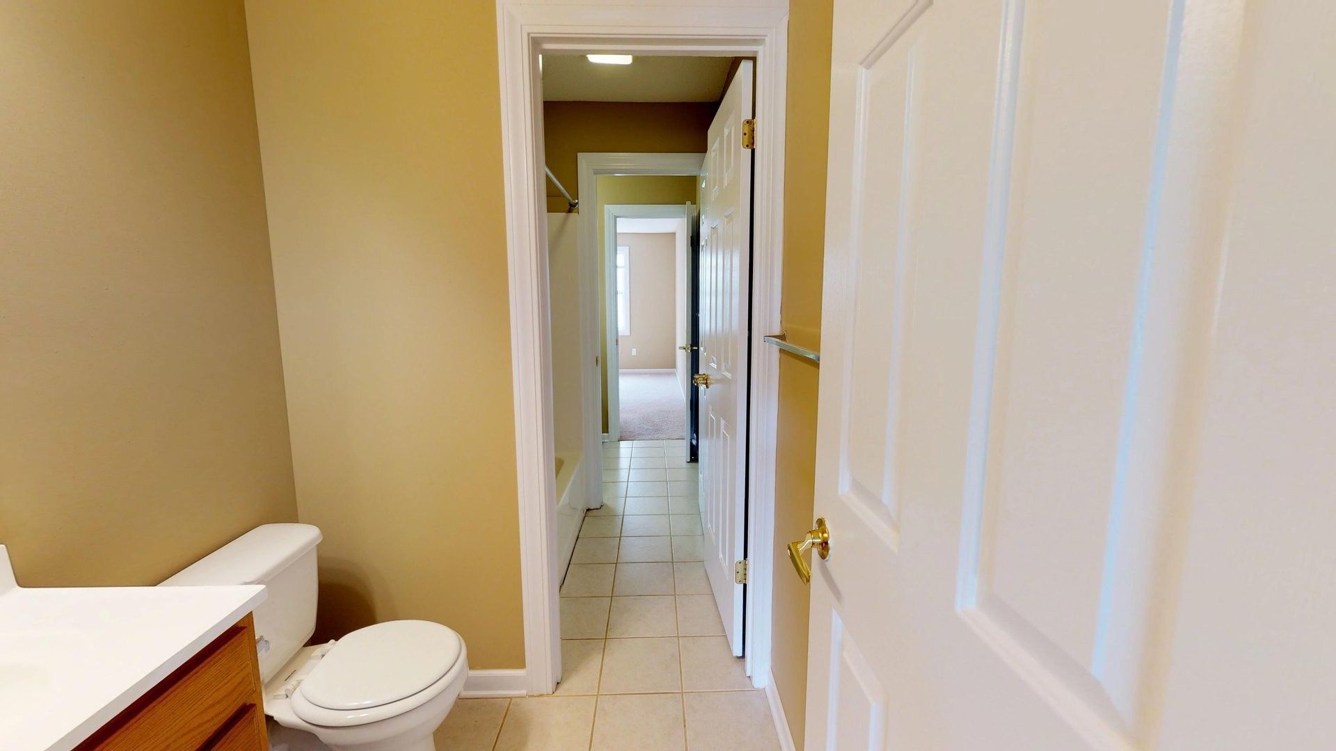 A bathroom with a toilet , sink , and door leading to a bedroom.