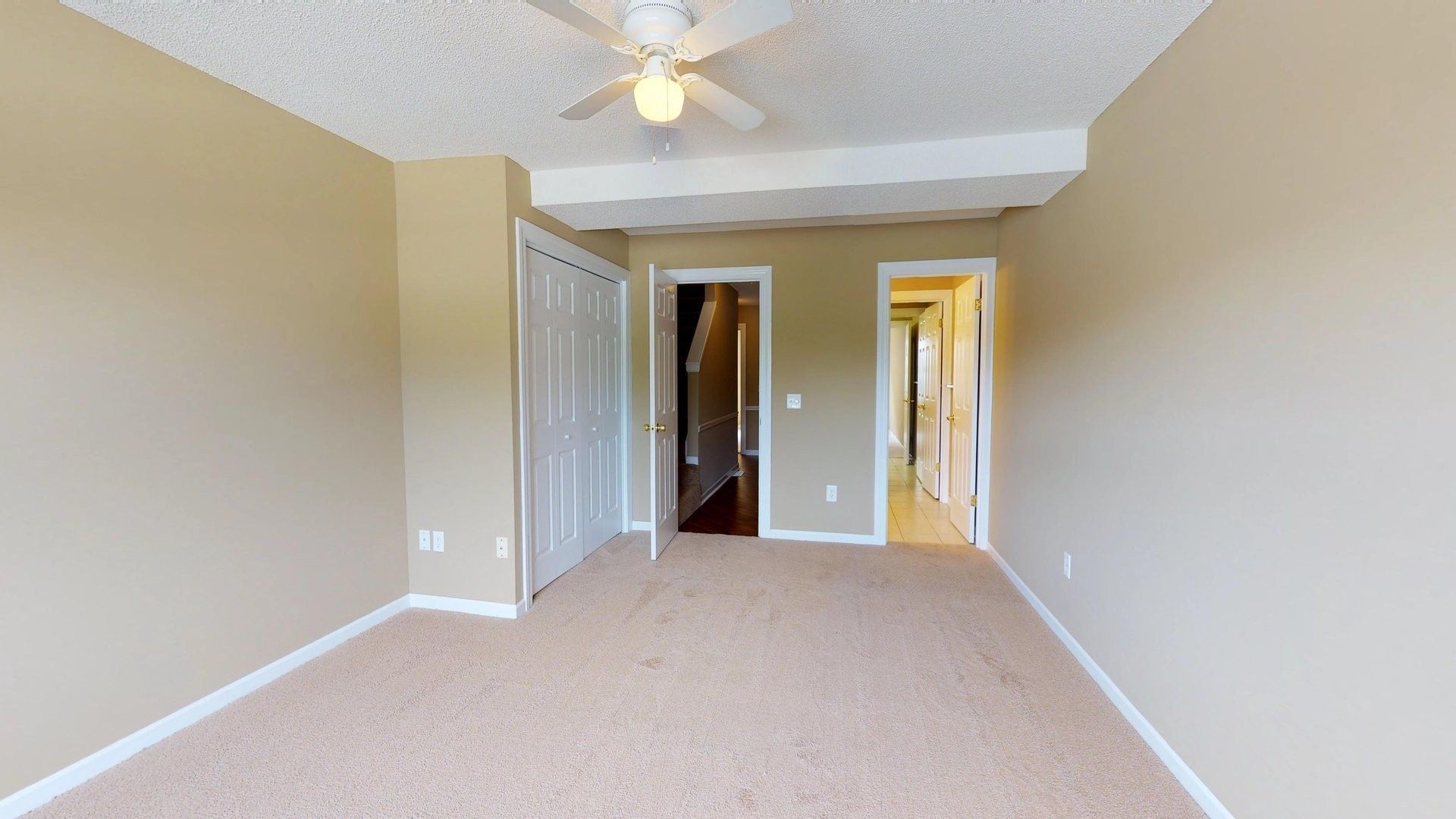 An empty bedroom with a ceiling fan and a closet.