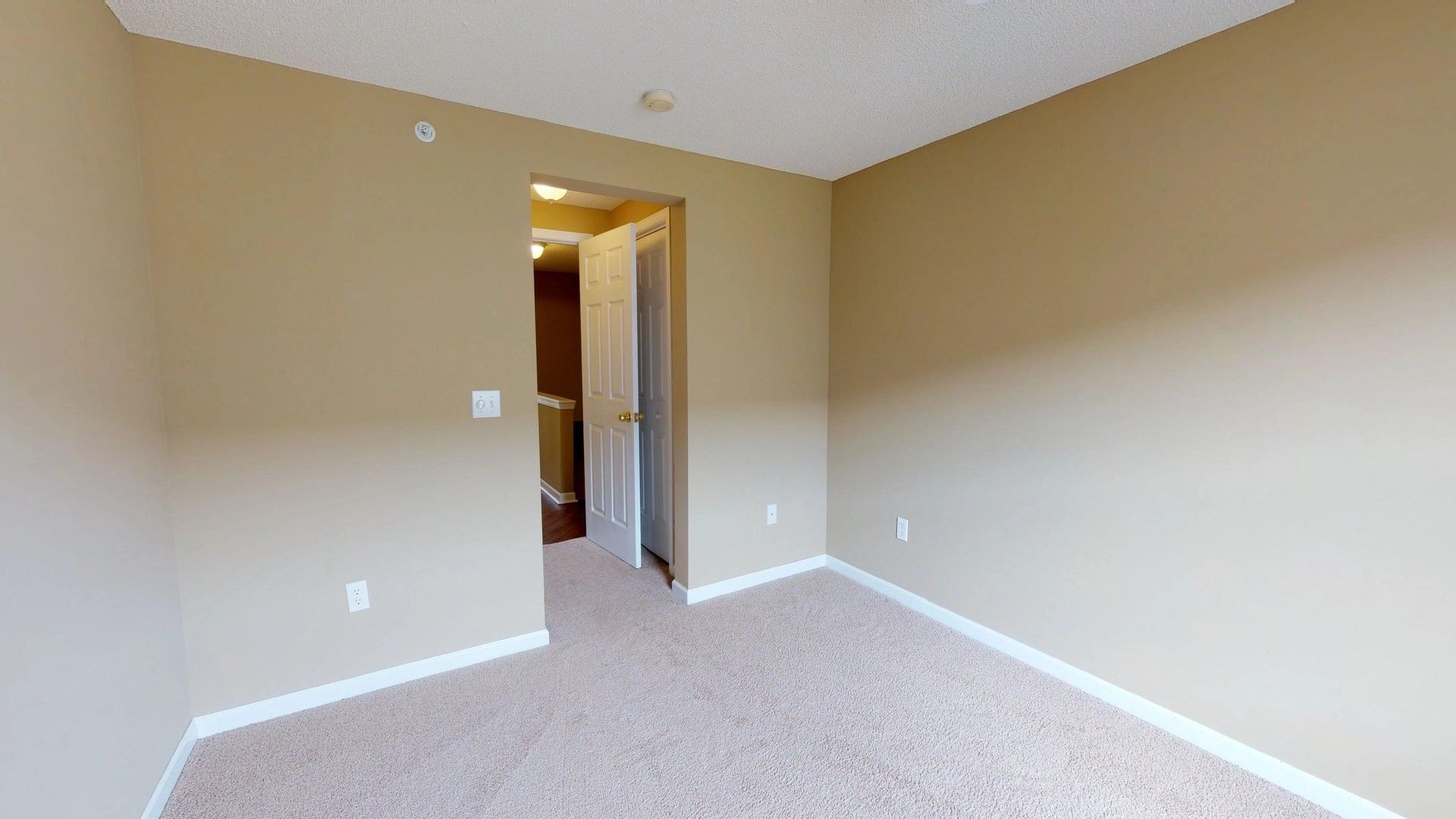 An empty bedroom with tan walls and a carpeted floor.