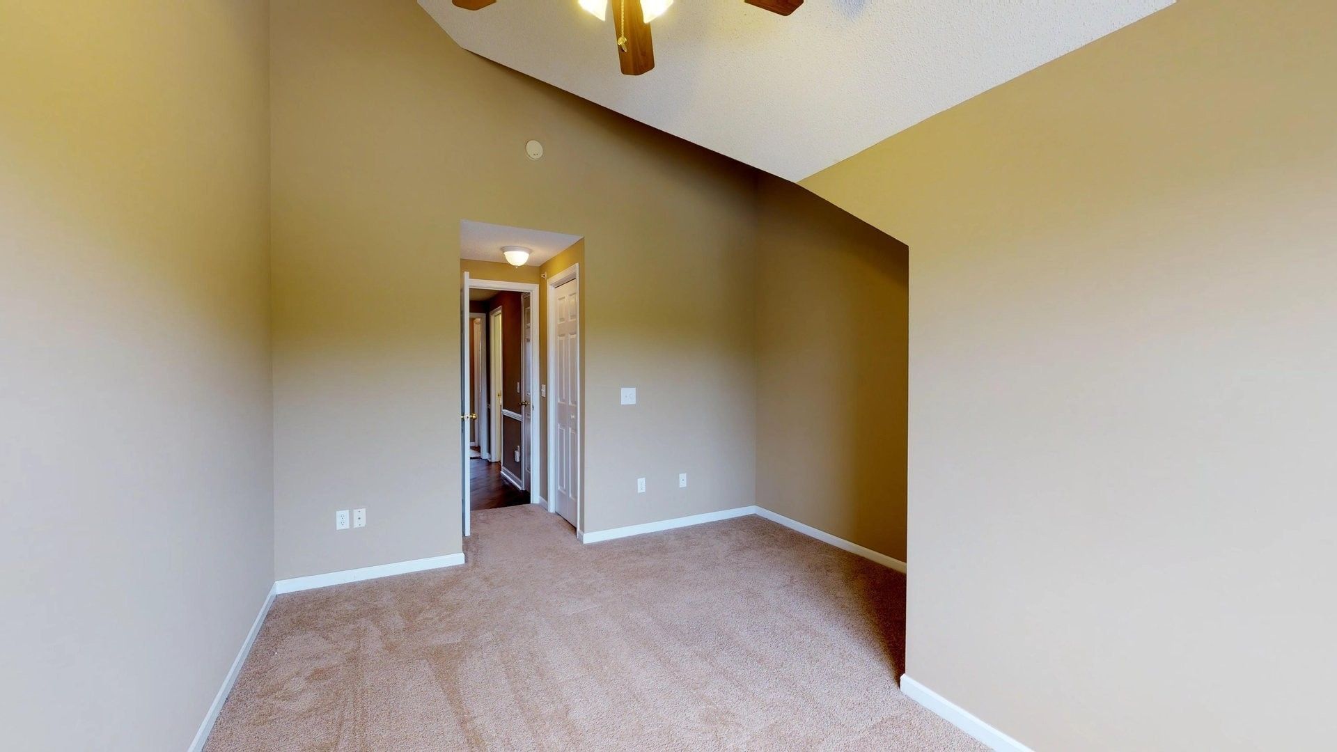 An empty bedroom with a vaulted ceiling and a ceiling fan.