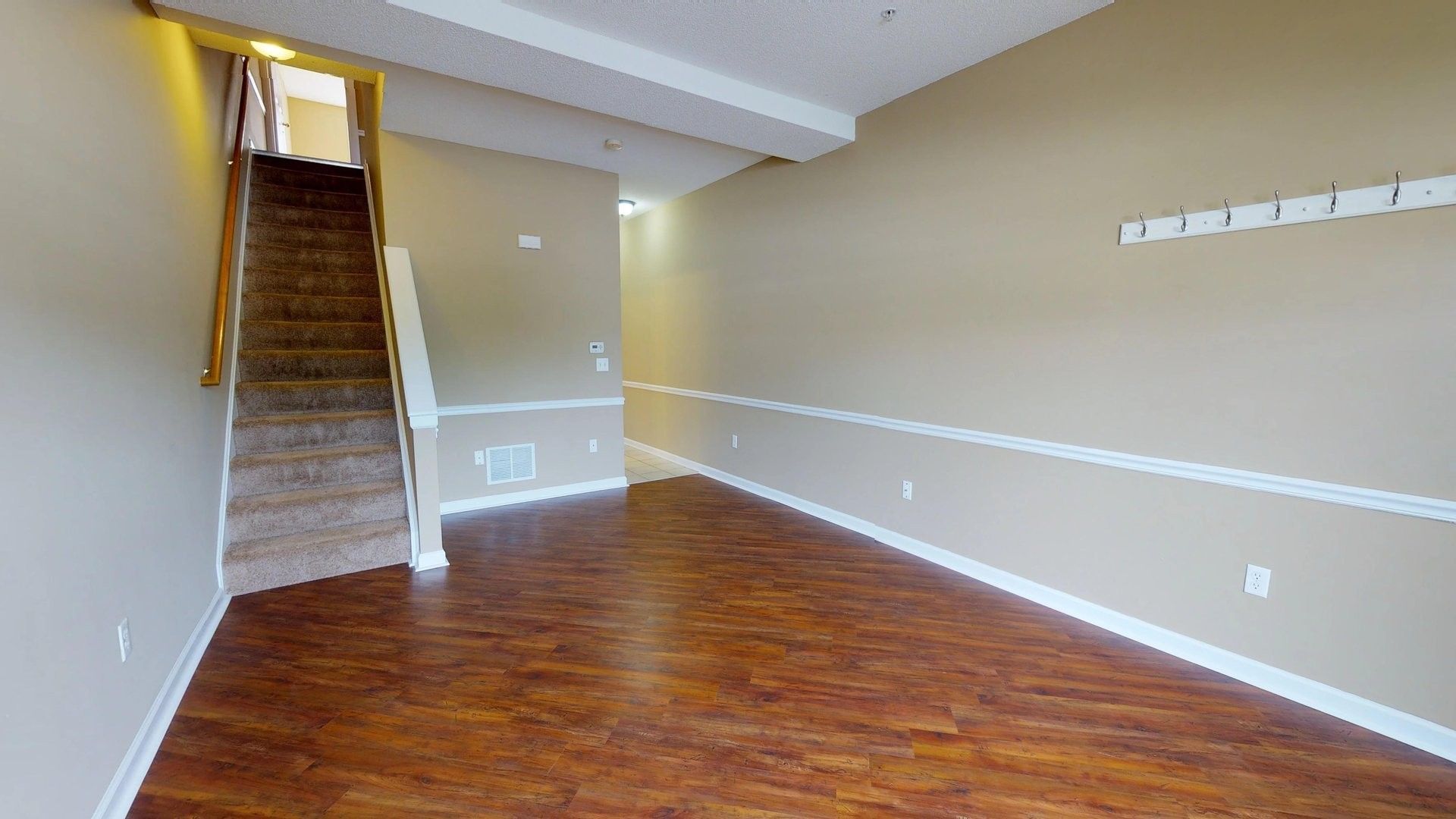 An empty living room with hardwood floors and stairs leading up to the basement.