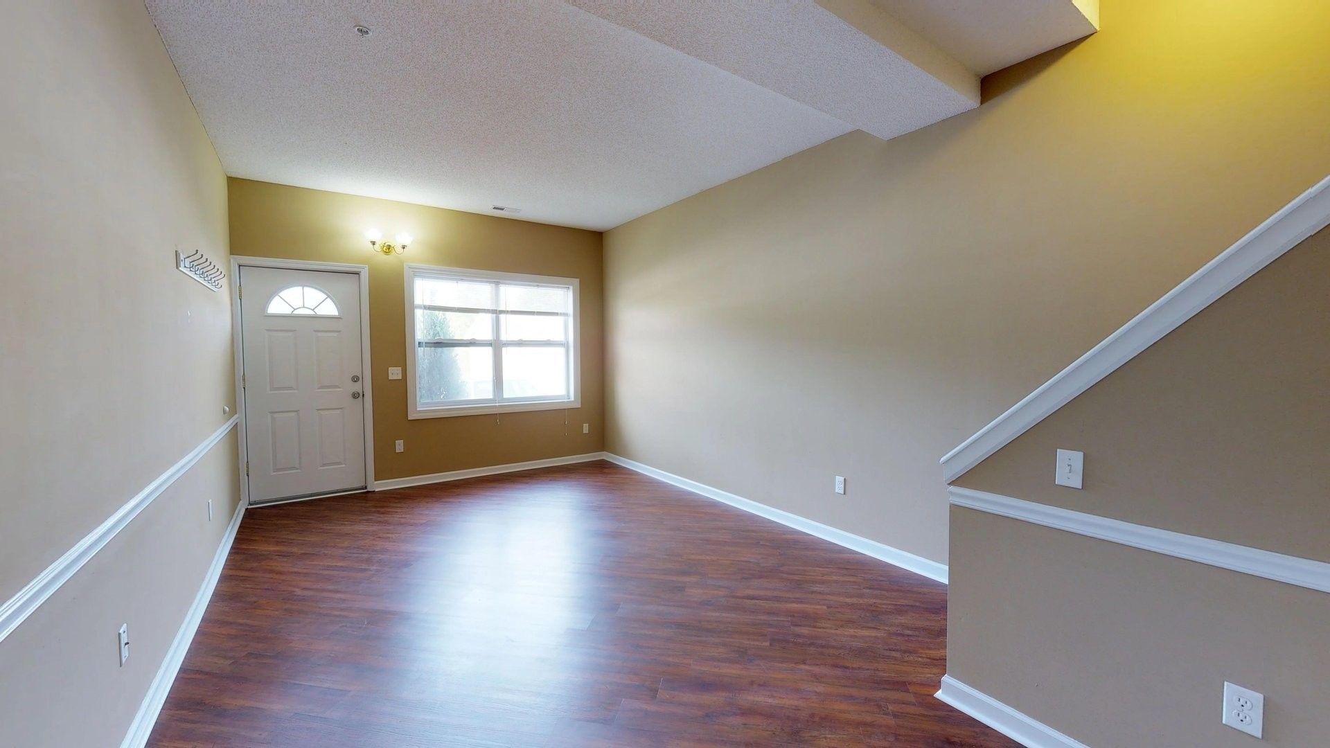 An empty living room with hardwood floors and stairs leading up to the second floor.