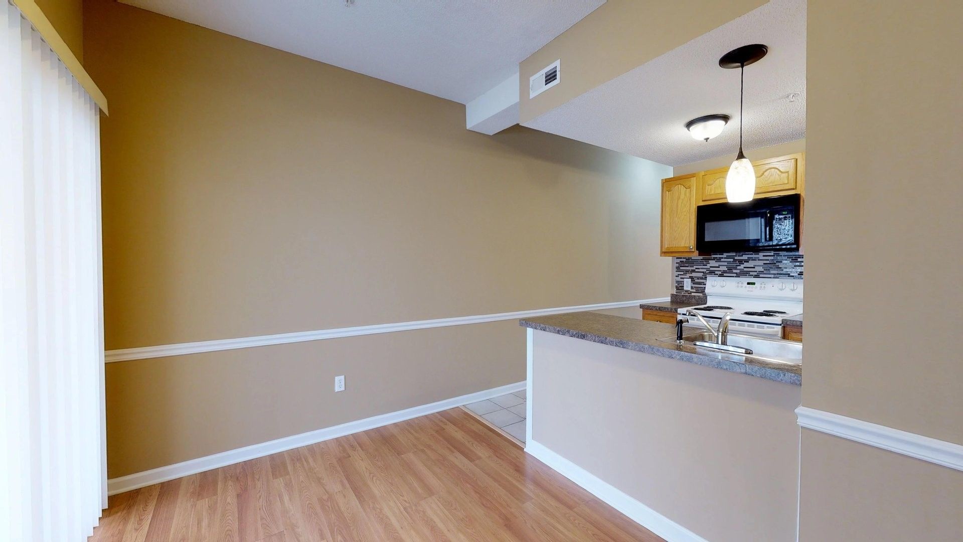 A living room with hardwood floors and a kitchen with sliding glass doors.