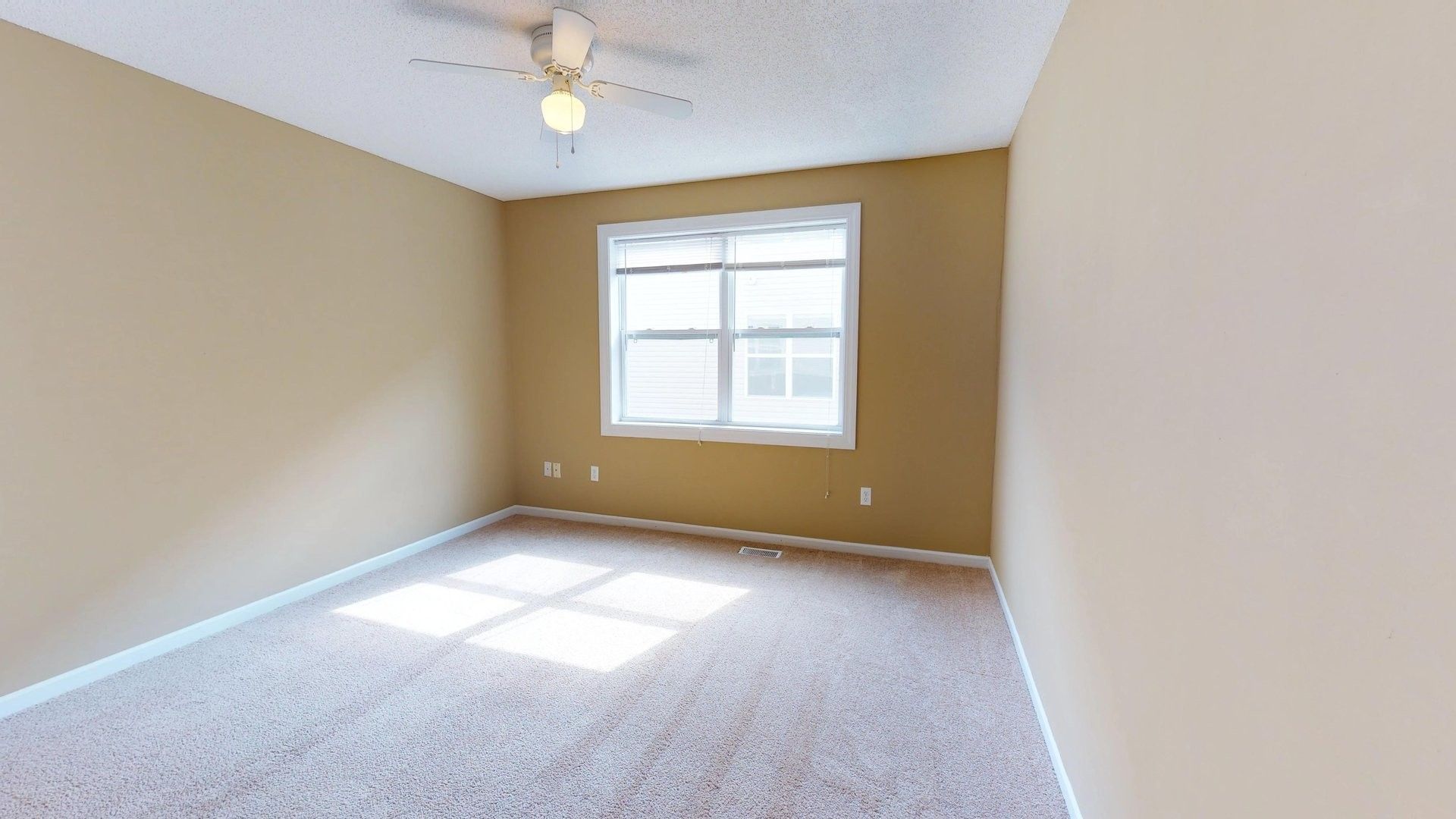An empty bedroom with a ceiling fan and a window.