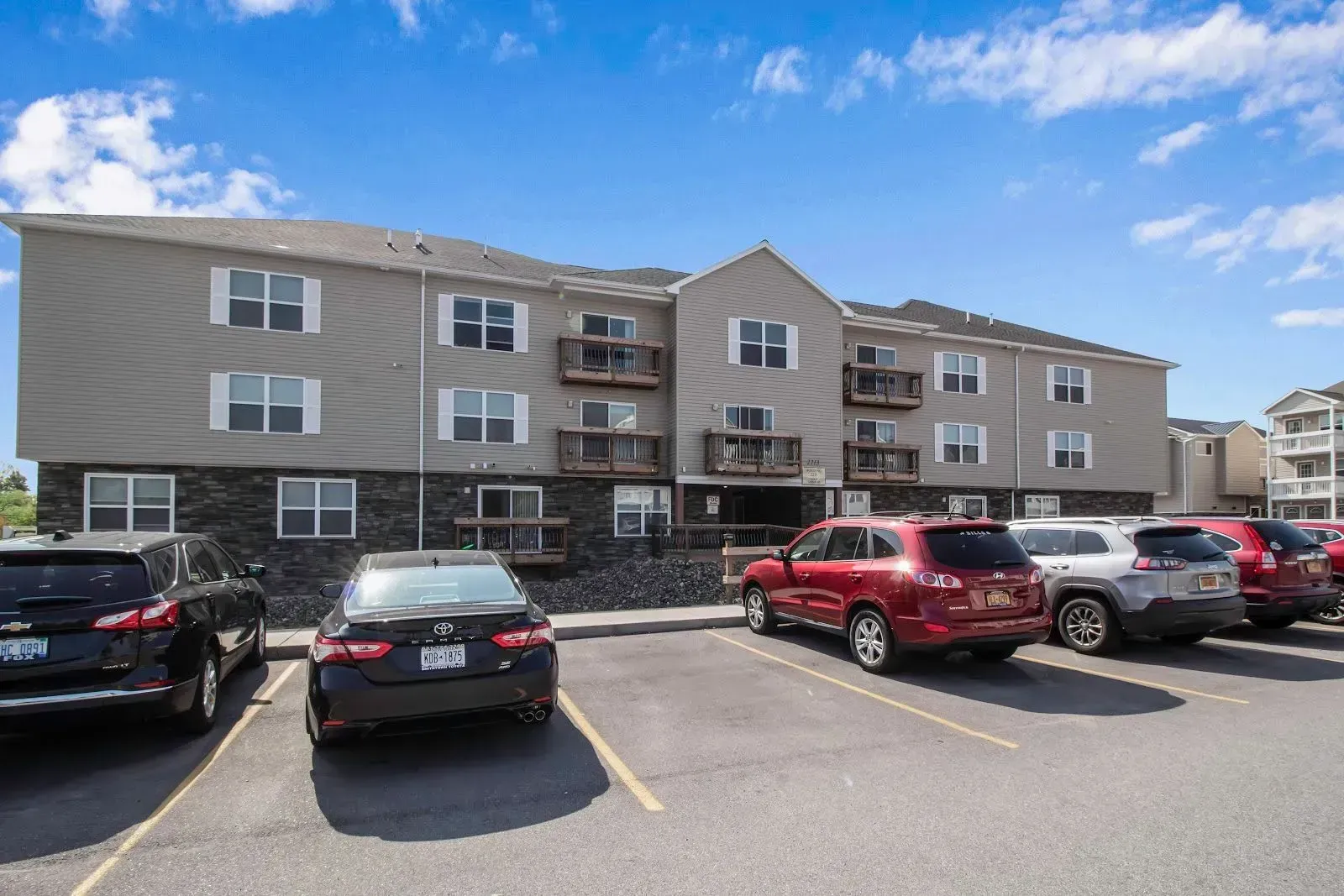A parking lot in front of a large apartment building with cars parked in front of it.