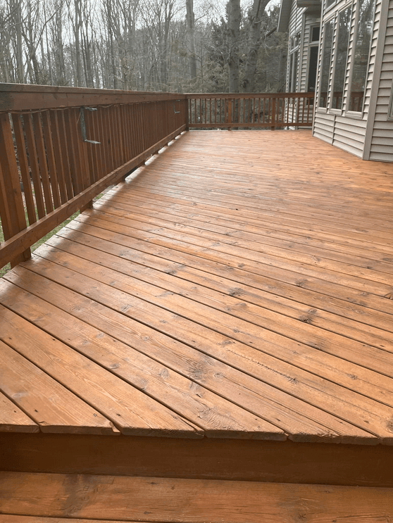 Wooden deck with railing, connected to a house. Exterior shot with natural lighting.