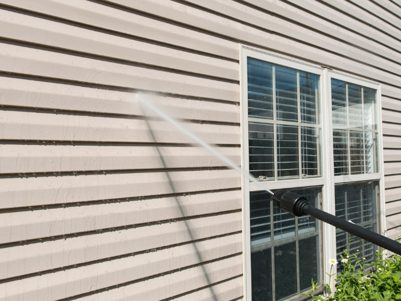 Pressure washing house siding next to a window; water spray visible.