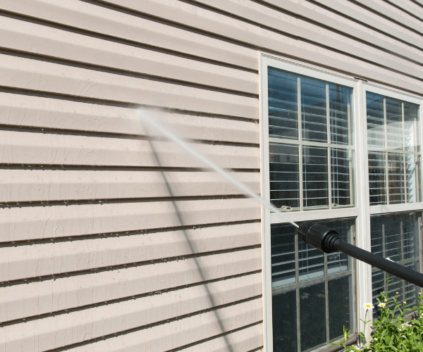 Pressure washing house siding next to a window; water spray visible.