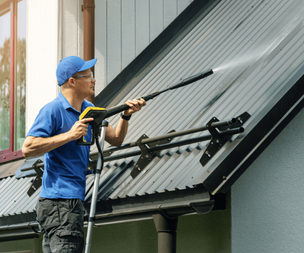 Man pressure washing a metal roof on a sunny day.