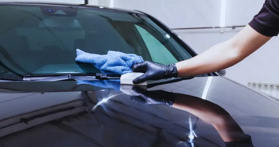 A man is polishing the door handle of a black car.