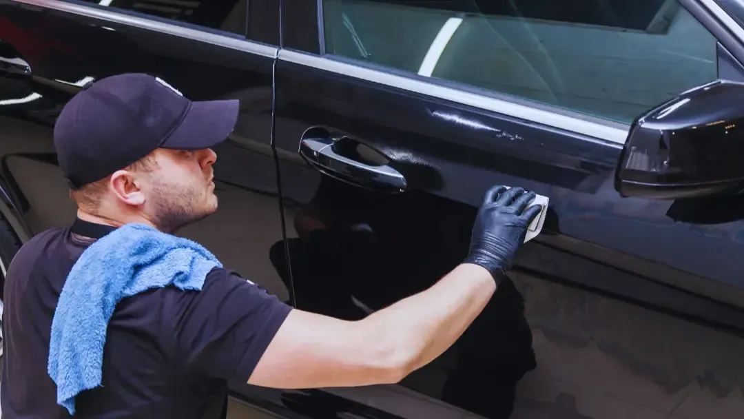 A man is polishing the door handle of a black car.