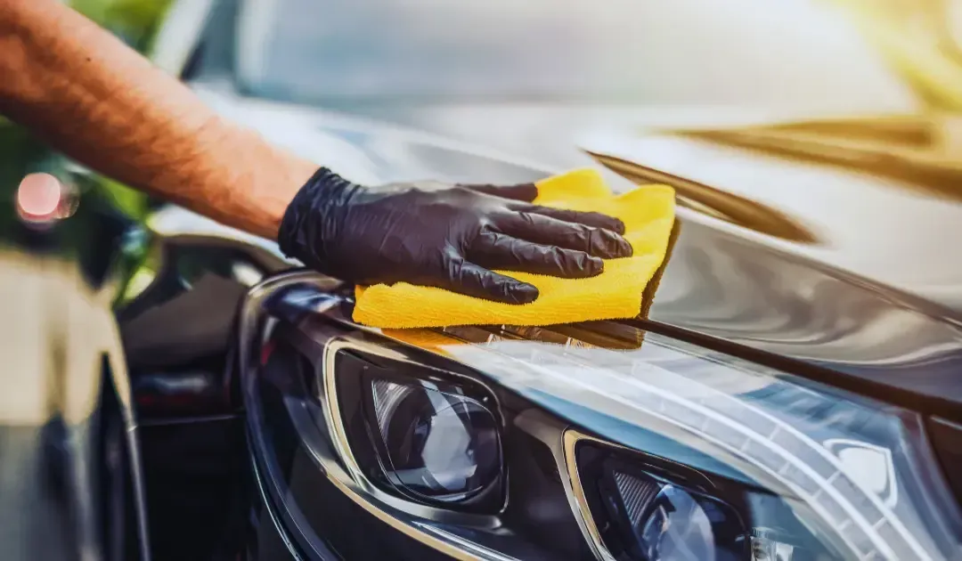 A person is cleaning a car with a yellow cloth.