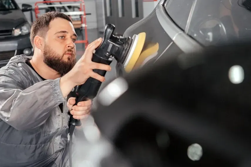 A man is polishing a car with a machine in a garage.