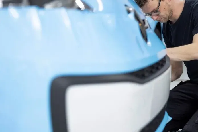 A man is working on the front of a blue car.