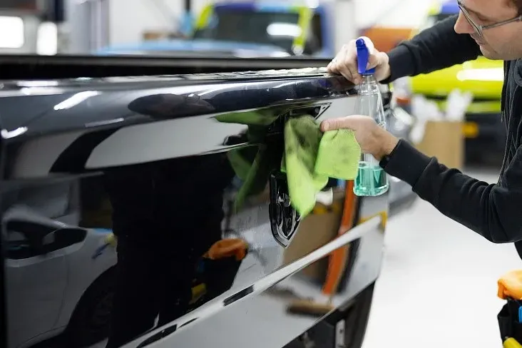 A man is cleaning a car with a cloth and spray bottle.