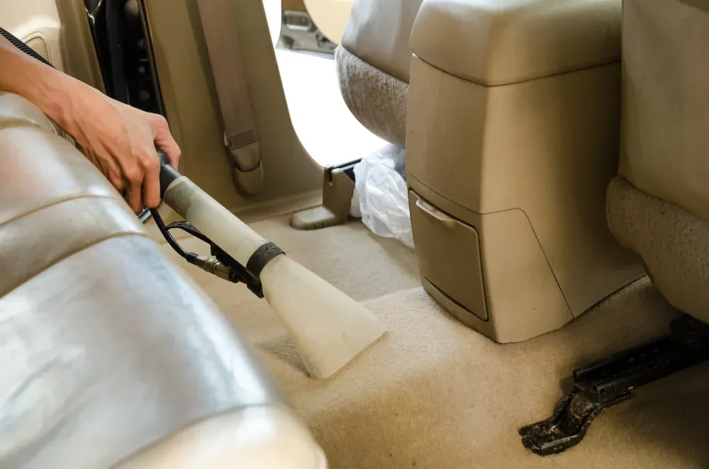 Mobile Detailing - A person is cleaning the back seat of a car with a vacuum cleaner.