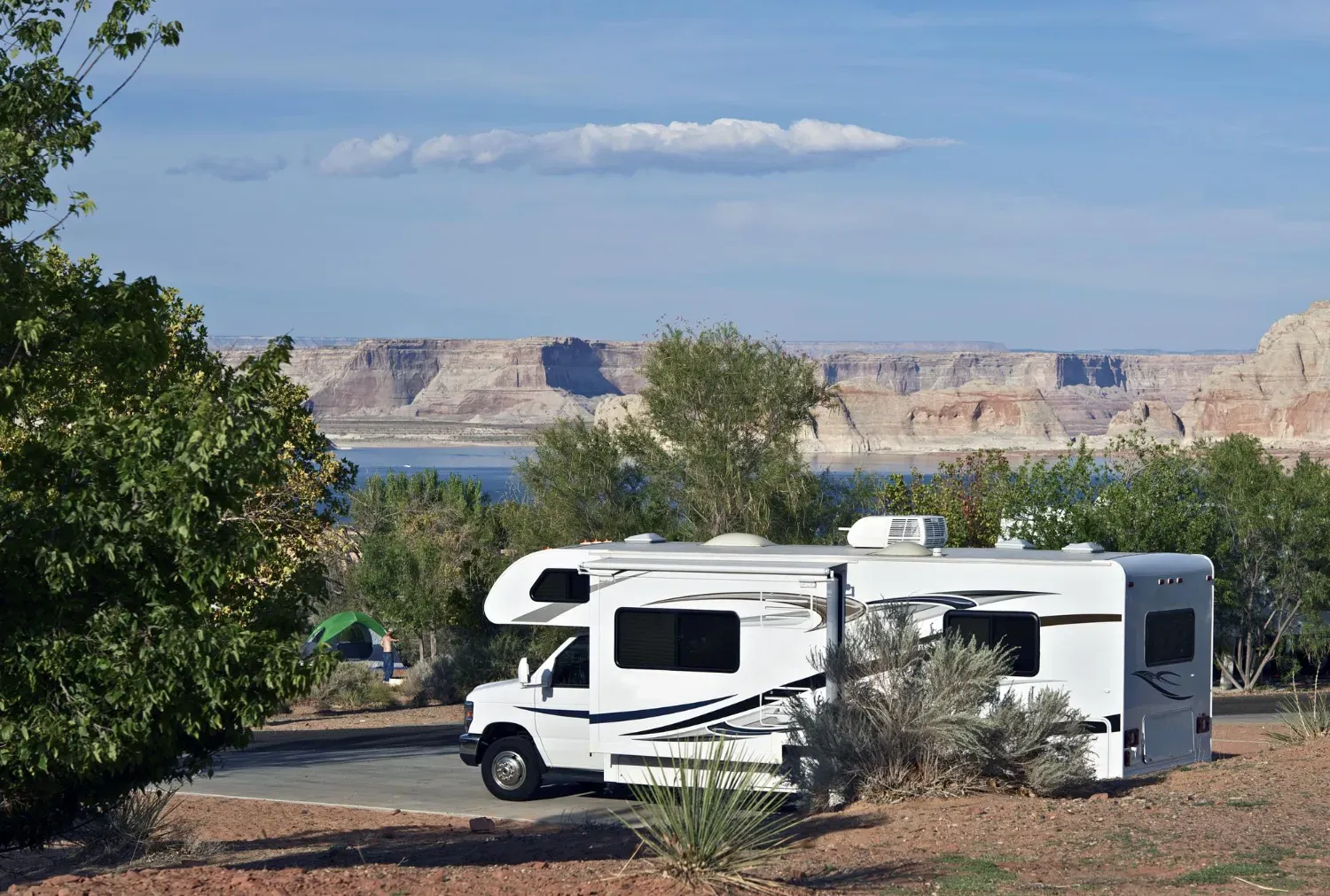 A white rv is parked in a parking lot next to a lake.