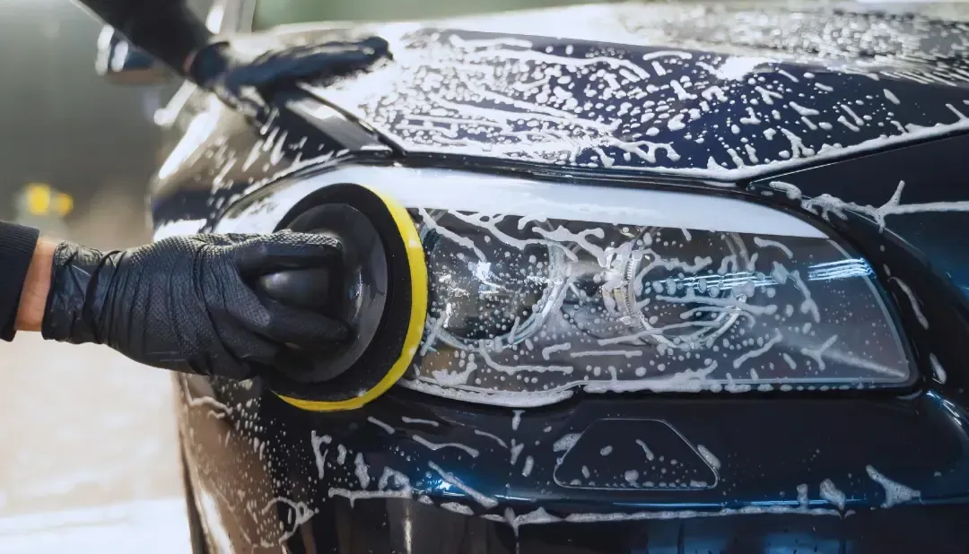 A person is polishing the headlight of a car with a polisher.