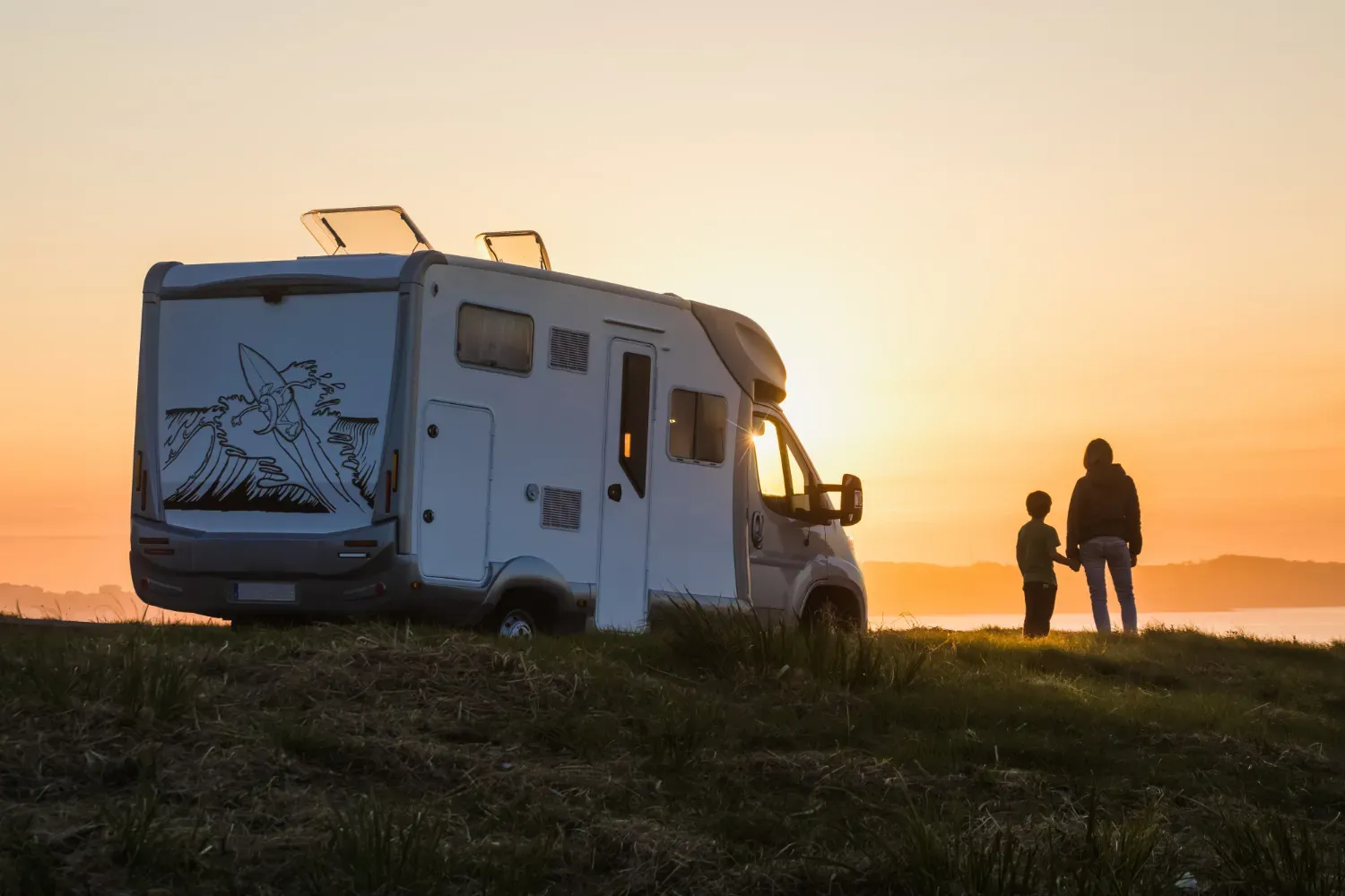 A man and a boy are standing in front of a rv at sunset.