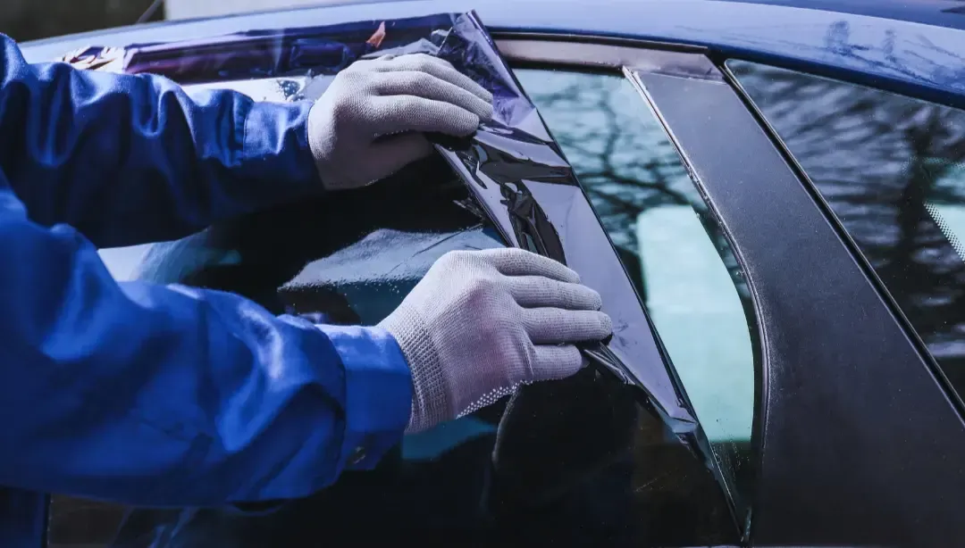 A man is applying tinted glass to a car window.