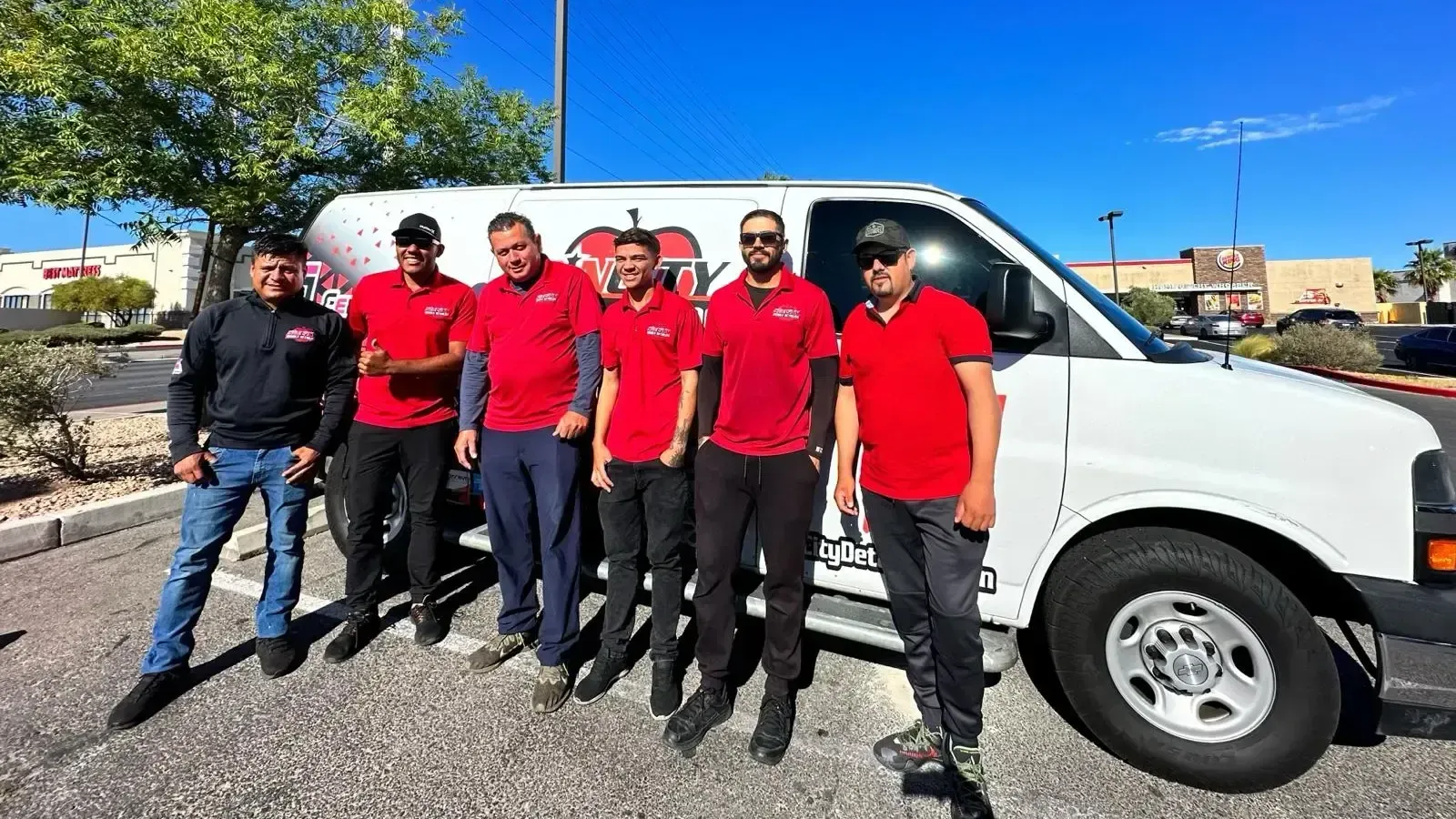a group of men in red shirts are standing in front of a white van .