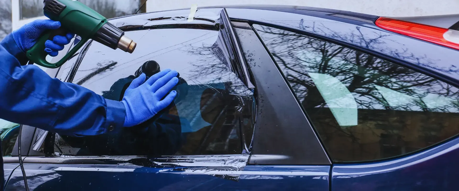 man putting window tint to a blue car