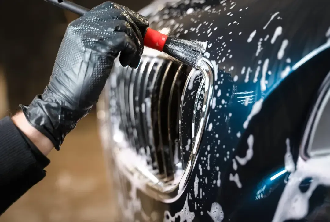 A person is cleaning the grille of a car with a brush.