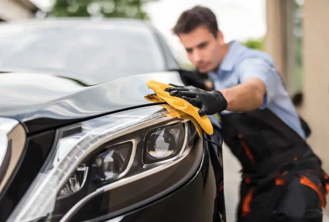 A man is cleaning a black car with a yellow cloth.