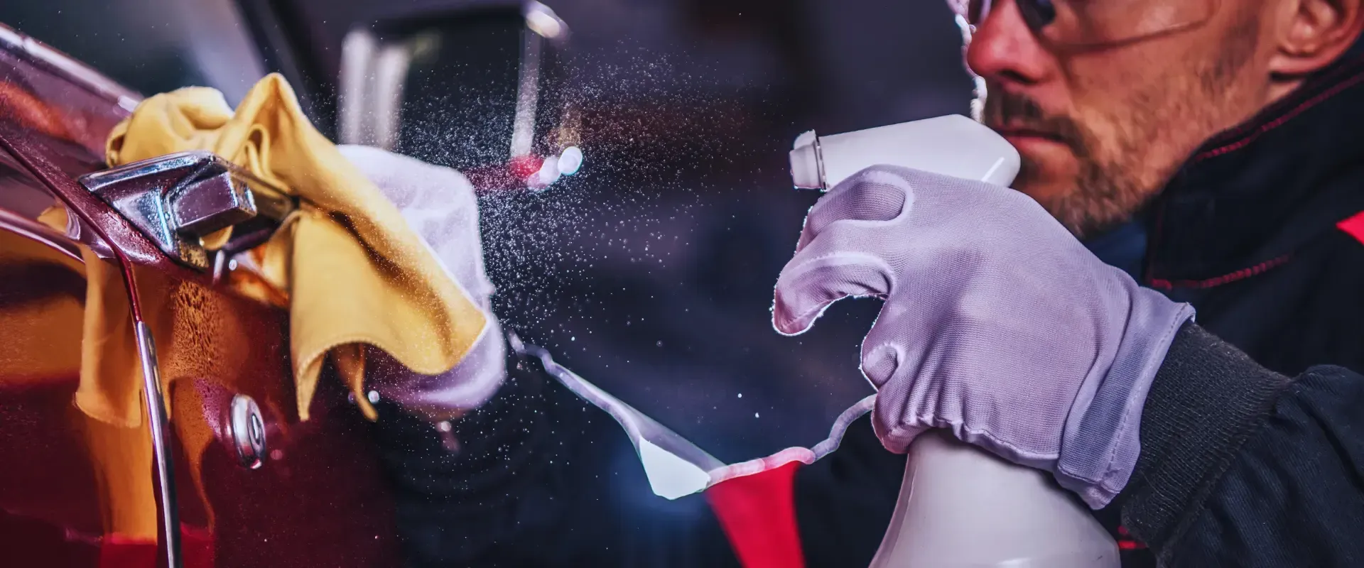A man is cleaning a car with a cloth and spray bottle.
