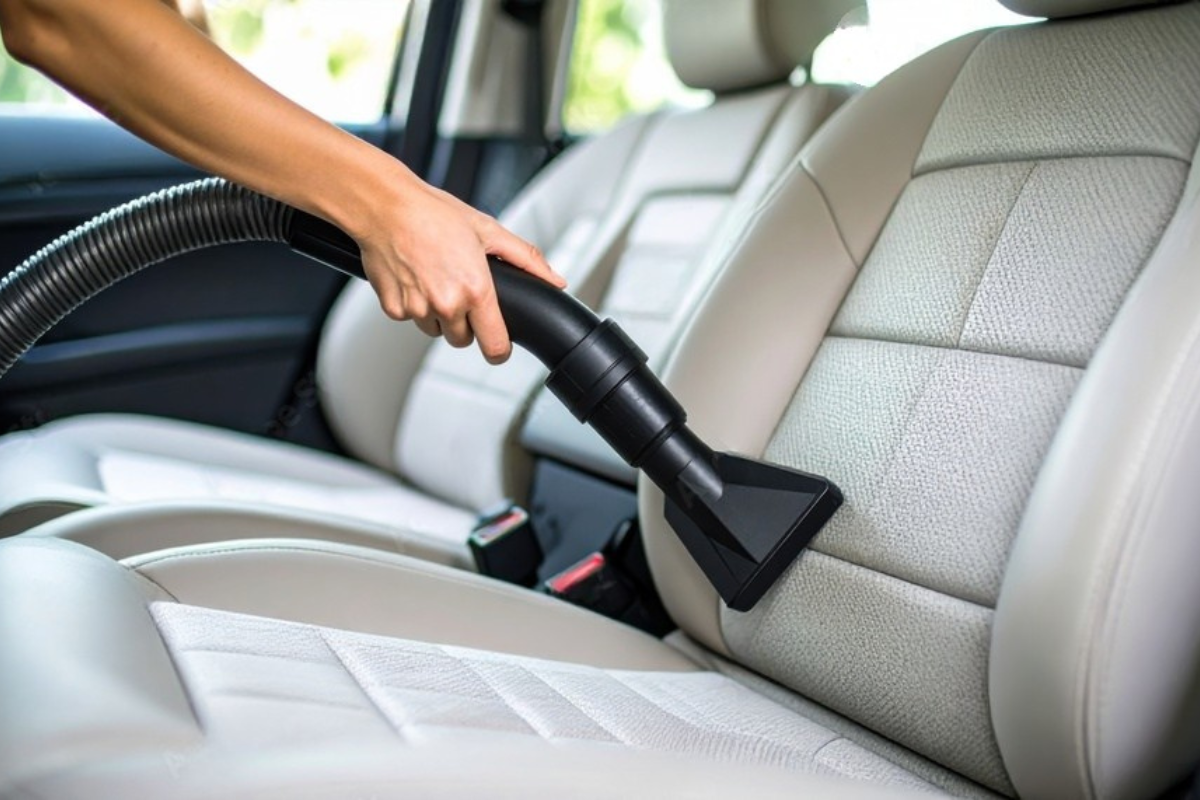 Person vacuuming a car seat with a handheld vacuum, close up.