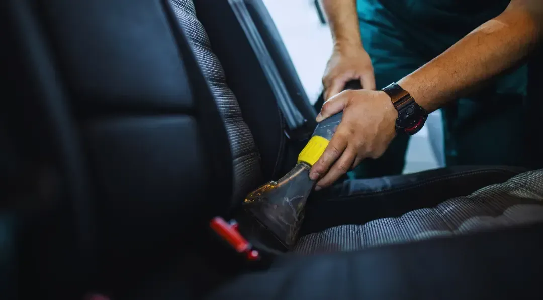 A man is cleaning the seats of a car with a vacuum cleaner.