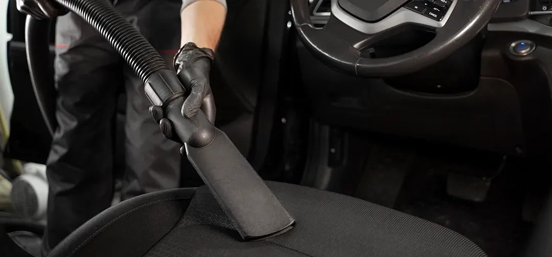 A person is cleaning a car seat with a vacuum cleaner.