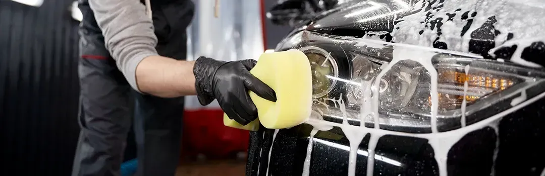 A person is washing a car with a sponge and soap.