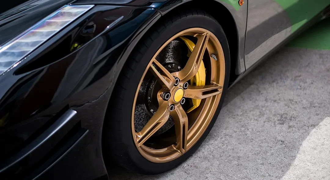 A black sports car with gold wheels is parked in a parking lot.