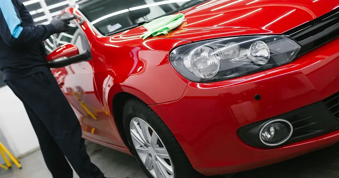 A man is cleaning a red car with a cloth.