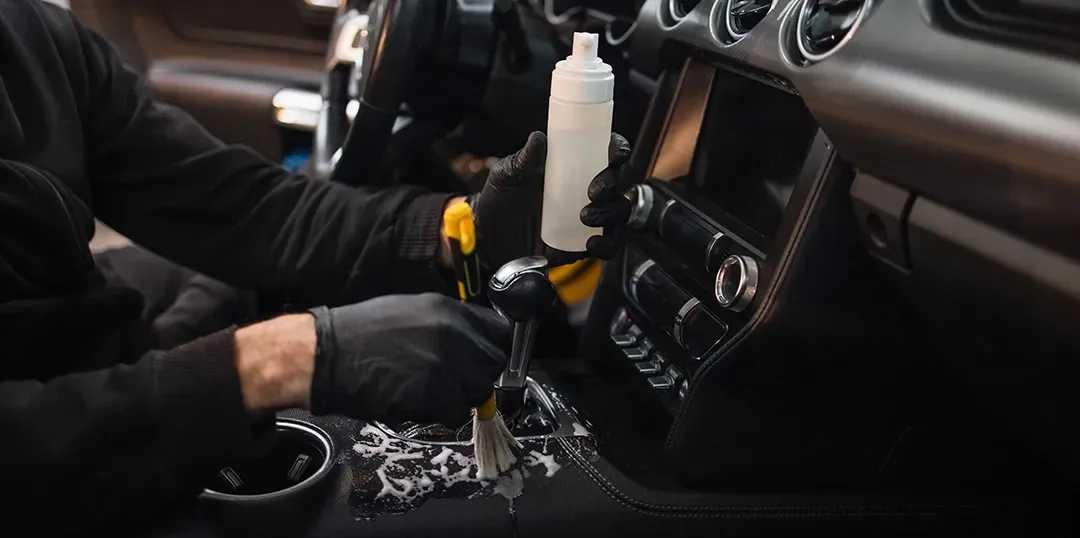 A man wearing black gloves is cleaning the interior of a car.