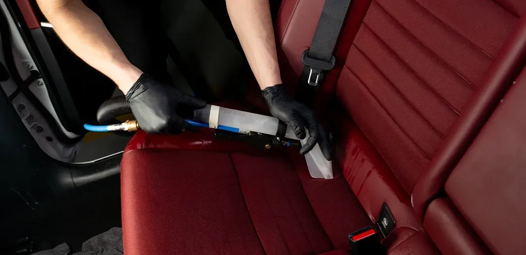 A person is cleaning the back seat of a car with a vacuum cleaner.
