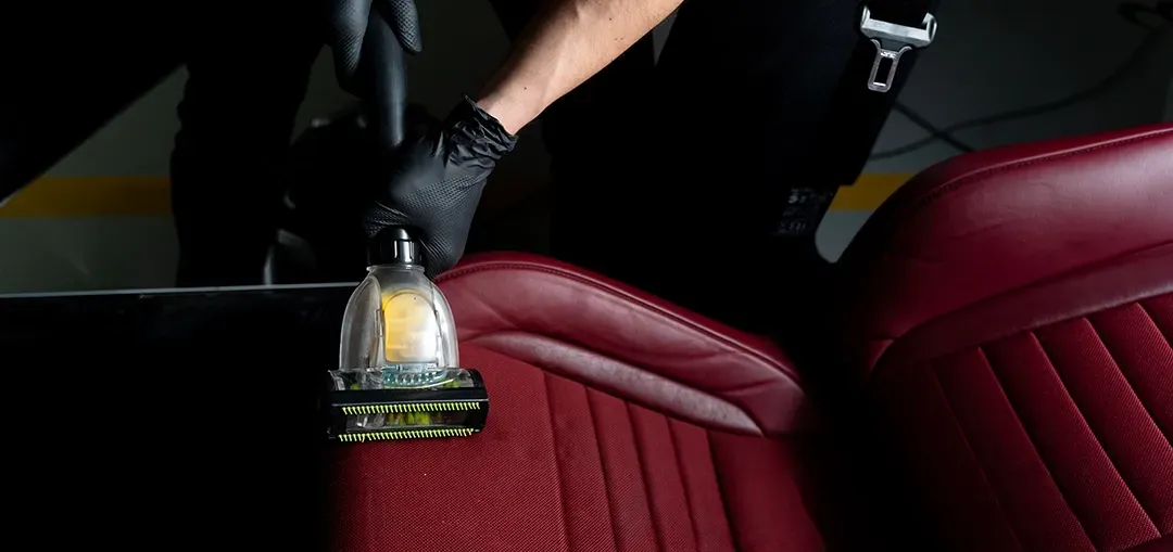 A person is cleaning a red leather car seat with a vacuum cleaner.