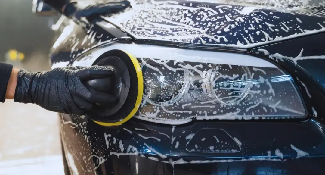A person is polishing the headlight of a car.