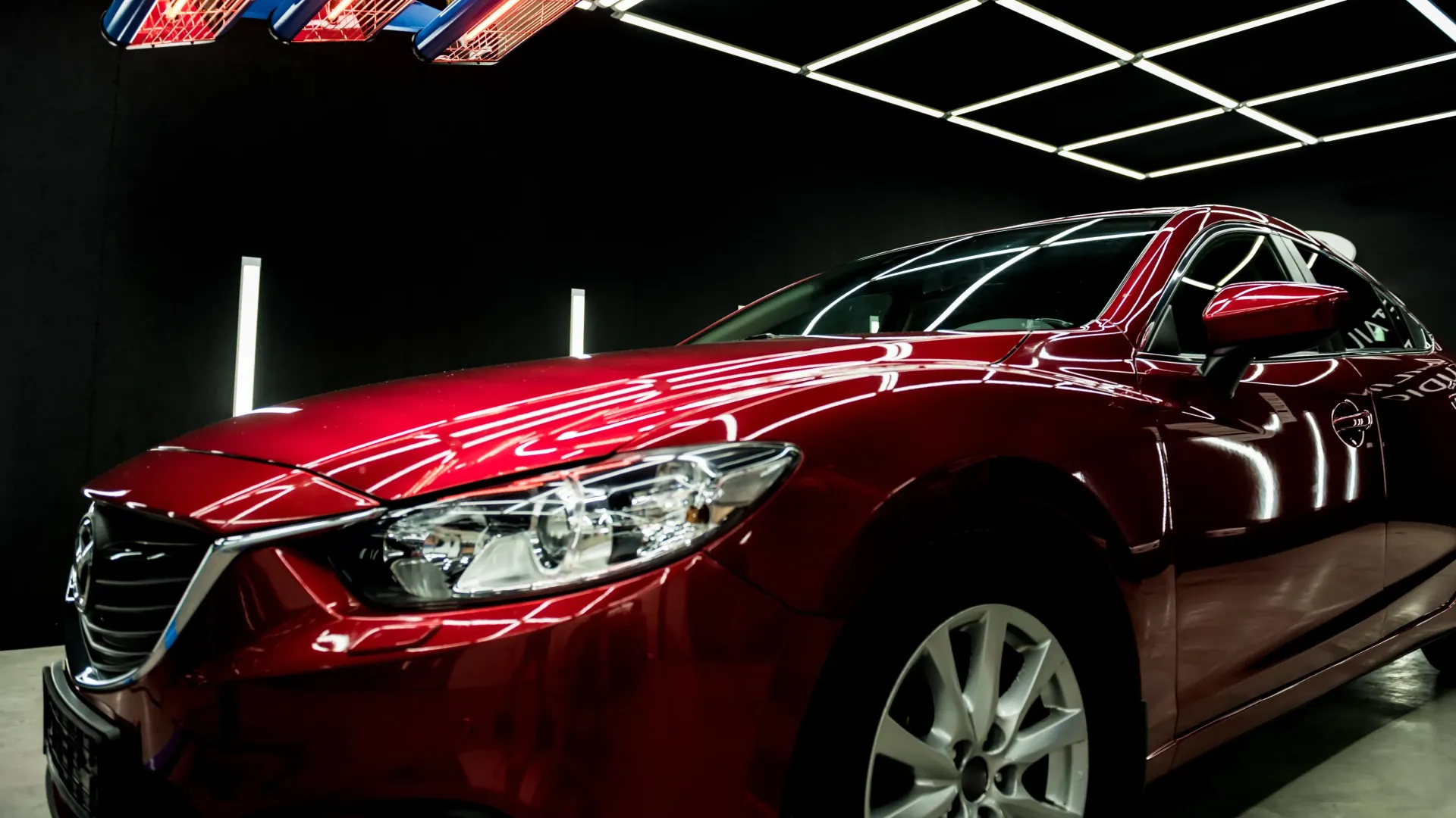 a red car is parked in a showroom under a ceiling light .